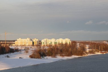 Güneşli bir akşamda nehir. Ağaçlar ve çalılar. Kış manzarası, nehir kıyıları çalılarla kaplı.