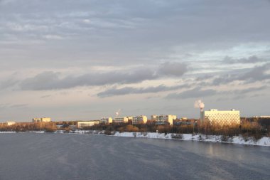 Güneşli bir akşamda nehir. Ağaçlar ve çalılar. Kış manzarası, nehir kıyıları çalılarla kaplı.