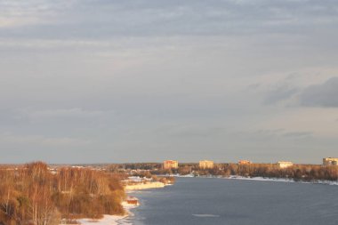 Güneşli bir akşamda nehir. Ağaçlar ve çalılar. Kış manzarası, nehir kıyıları çalılarla kaplı.