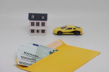 Yellow envelope with banknotes on the background of a toy house and a car, plans for the future