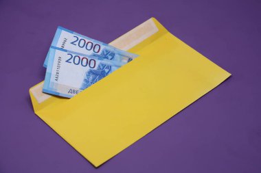 Banknotlar mor arka planda sarı bir zarfın içinde. Rüşvet konsepti. Maaşlar zarflarda. Finansal dolandırıcılık. Kapat.