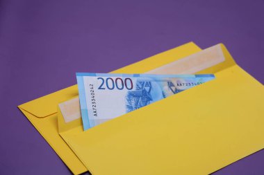 Banknotlar mor arka planda sarı bir zarfın içinde. Rüşvet konsepti. Maaşlar zarflarda. Finansal dolandırıcılık. Kapat.