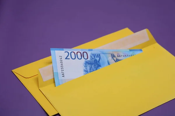 Banknotlar mor arka planda sarı bir zarfın içinde. Rüşvet konsepti. Maaşlar zarflarda. Finansal dolandırıcılık. Kapat.