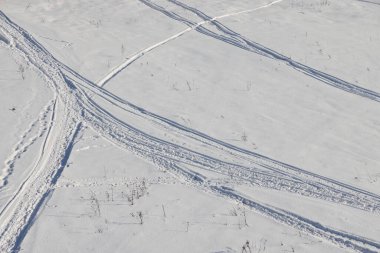 Issız kış manzarası. Saf beyaz kar üzerinde bir ayak izi yolu uzanıyor. Çalı dalları kardan sarkıyor. Kar manzarasında ayak izleri