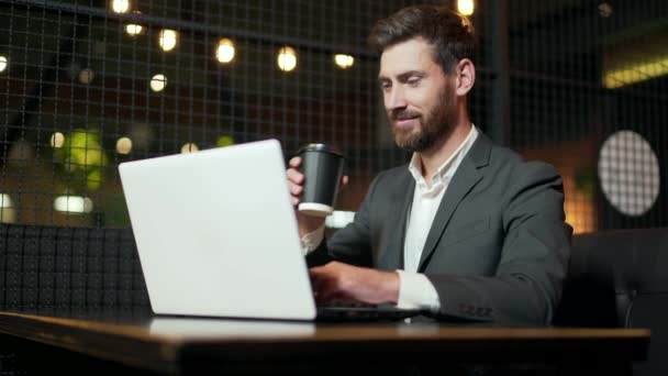 在酒店餐厅或室内咖啡店休息期间工作的成功的白人商人 拥有现代深色背景的英俊大胡子商人 带着手提电脑咖啡杯 自助餐厅的自由职业者 — 图库视频影像