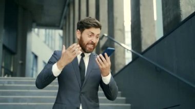 Kızgın erkek işadamı dışarıda telefonda konuşurken ağlıyor. Dışarıdaki çağrıda bağırıyor. Akıllı telefondan sinirli, profesyonel bir konuşma. Sinirli çalışan çığlığı Kentsel caddede konuşuyor.