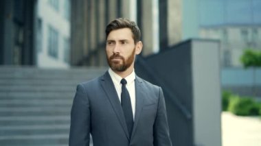 Portre genç kendinden emin beyaz sakallı iş adamı kameraya bakıyor ciddi bir iş adamı kentsel arka planda duruyor modern ofis binası açık havada resmi bir takım elbise