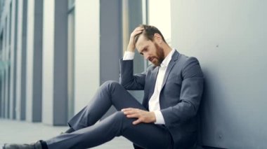 Hüzünlü girişimci resmi takım elbiseli işçi modern ofis merkezinin yakınındaki açık hava caddesinde oturuyor. Mali kriz nedeniyle işsiz kalan erkek işadamının sorunları var. dışarıName
