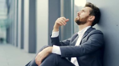 Hüzünlü girişimci resmi takım elbiseli işçi modern ofis merkezinin yakınındaki açık hava caddesinde oturuyor. Mali kriz nedeniyle işsiz kalan erkek işadamının sorunları var. dışarıName