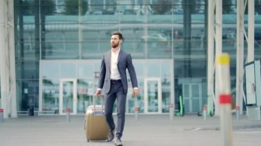 Beyaz sakallı turist işadamı şehir arka planında bir şehir sokağında bavulla toplu taşıma binasında yürüyor. Resmi takım elbiseli adam. İş gezgini havaalanı terminalinde bavulu çekiyor.