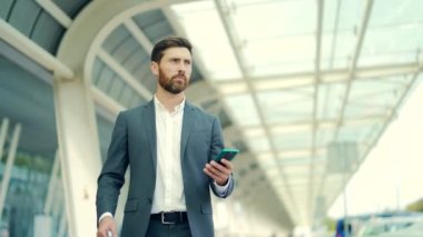 İş adamı arka planda duruyor modern bir tren istasyonu havaalanı ya da resmi takım elbiseli otobüs durağı uygulamalı cep telefonu kullanan seyahat eden akıllı telefonlu bir iş adamı bir taksi çağırır.