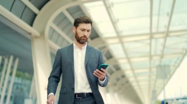 İş adamı arka planda duruyor modern bir tren istasyonu havaalanı ya da resmi takım elbiseli otobüs durağı uygulamalı cep telefonu kullanan seyahat eden akıllı telefonlu bir iş adamı bir taksi çağırır.
