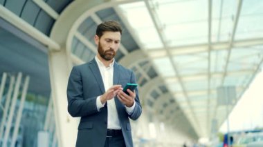 Arka planda duran iş adamı resmi kıyafet giymiş modern bir tren istasyonu havaalanı uygulamalı cep telefonu kullanıyor. Dışarıda akıllı telefonu olan gezgin iş adamı turist. çalışan açık havada