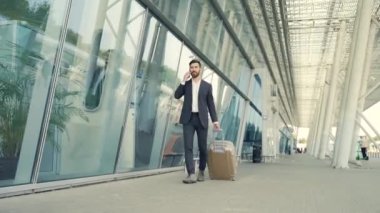 Beyaz sakallı turist işadamı şehir arka planında bir şehir sokağında bavulla toplu taşıma binasında yürüyor. Resmi takım elbiseli adam. İş gezgini havaalanı terminalinde bavulu çekiyor.