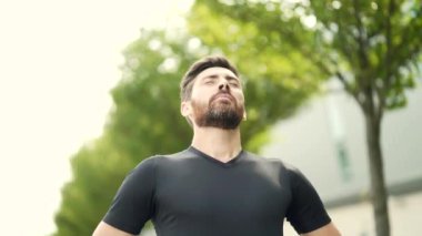 Portre mutlu bir adam doğada duruyor rahatlıyor, temiz hava soluyor gözlerini kapatıyor koşudan ya da şehir parkında antrenmandan sonra erkeğin keyfini çıkarıyor. Akıllı saat fitness takip bilekliği arıyor ve kullanıyor