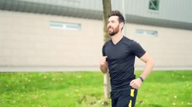Beyaz sakallı, mutlu bir koşucu şehir parkının arka planında koşuyor. Sabah koşusu. Aktif sağlıklı yaşam tarzı uygunluğu. Dışarıda spor antrenmanı. Sporcu eğitim koşusu egzersizi