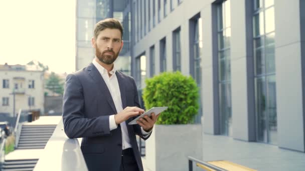 穿着正式西装的时髦大胡子商人手握平板电脑 站在室外现代写字楼的背景上 男子使用智能手机或使用手机室外城市街道 — 图库视频影像