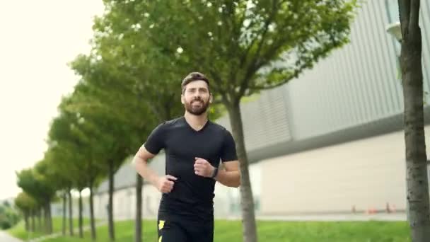 年轻的白种人留着胡子 快乐的男子跑步者在城市公园的城市背景下沿着街道慢跑 早上慢跑 积极健康的生活方式 户外运动 田径训练跑练习 — 图库视频影像