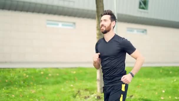 若い白人の髭を生やした幸せな男が 都会の公園を背景に通りをジョギングしている 朝のジョギング アクティブな健康的なライフスタイルフィットネス スポーツワークアウト屋外 アスリートトレーニング実行演習 — ストック動画