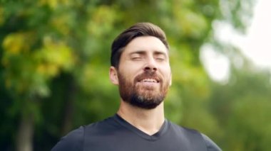 Kapalı portre genç mutlu sakallı adam ormanda ağaçların arasında duruyor rahatlıyor, gözlerini kapatarak temiz hava soluyor. Erkek, huzur dolu, parkta sakin bir hayatın tadını çıkarır. Açık havada. Mutluluk
