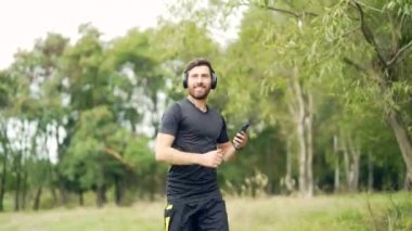 Genç, neşeli, aktif, kulaklıkla koşan, müzik dinlemekten, şehir parkında ya da orman geçmişinde koşmaktan keyif alan genç bir adam. Erkek koşucu spor kulaklıkları yapıyor.