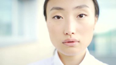 Kapalı alanda ya da dışarıda bulanık bir arkaplanda kameraya bakan güzel bir kadının yakın plan yüzü. Beyaz giysili çekici bir kızın portresi. Kapat.