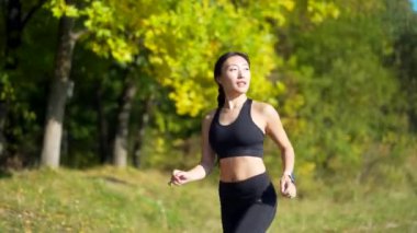 Genç Asyalı mutlu kadın koşucu ormanda ya da şehir parkında koşuyor. Sabah koşusu. Aktif sağlıklı yaşam tarzı. çekici fitness dişisi. Dışarıda spor antrenmanı. Atletizm antrenmanı temiz havada yapılır.