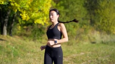 Genç Asyalı mutlu kadın koşucu ormanda ya da şehir parkında koşuyor. Sabah koşusu. Aktif sağlıklı yaşam tarzı. çekici fitness dişisi. Dışarıda spor antrenmanı. Atletizm antrenmanı temiz havada yapılır.