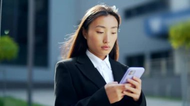 Asyalı bir çalışan şehir merkezindeki modern ofis binasının arka planında cep telefonuna mesaj atıyor. İş kadını resmi bir takım elbiseyle şehrin dışındaki akıllı telefondan mesaj atıyor.