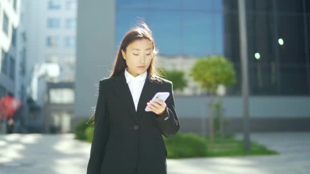 スーツ姿のビジネスウーマンや大学生が街中を歩き 携帯電話やスマートフォンを使って話をしています アジアの若い女性のオフィスワーカー彼の手に携帯電話を持つ従業員 — ストック動画