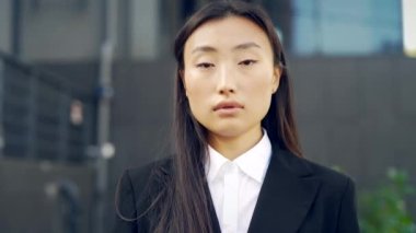 Kentin arka planında kameraya bakan Asyalı genç iş kadınının yakın plan portresi. Kendine güvenen bağımsız bir iş kadını ya da öğrencisinin yüzü. - Dışarıda. Açık havada. Yakın çekim.
