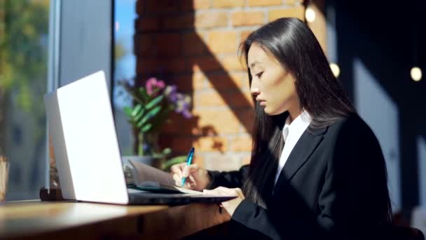young female freelancer or student working online or studying remotely in a cafe. Asian business woman in suit uses typing laptop at workplace in coworking hot desk. writes in a notebook. Learn