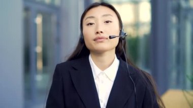 Asyalı iş kadınının portresi ofis çalışanı konuşuyor ve kulaklıkla kameraya bakıyor. Bayan müdür bir konuşma yapıyor. Konferans toplantısı. Yardım merkezi ya da yardım hattı. Web kamerası görünümü