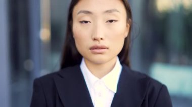 Kentin arka planında kameraya bakan Asyalı genç iş kadınının yakın plan portresi. Kendine güvenen bir iş kadını ya da öğrencinin yetişkin haliyle yüzleşmek. - Dışarıda. Açık havada. Yakın çekim.