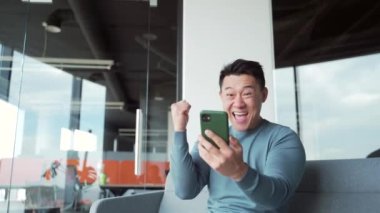 Mutlu Asyalı serbest çalışan, çalışan, gezici kazananı kutlayan mutlu mutlu Asyalı adam, çok sevinçli şanslı kazanan mesajda iyi haberler alıyor. Akıllı telefon kullan. Finansal başarı için ofis zaferine oyna.