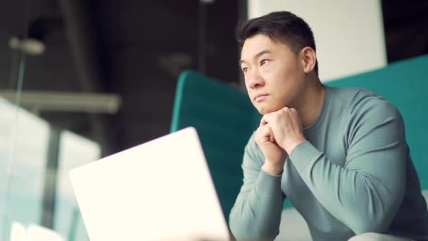 現代的なオフィスデスクでラップトップコンピュータで作業している思慮深い若いアジアのフリーランスの肖像画 自信を持って集中的な男性起業家室内 インスピレーションが問題を解決すると考えています スタートアップ — ストック動画