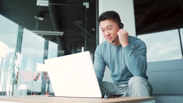 アジア系男性のフリーランスは 現代オフィスの同僚の会議室で同僚と話しています ノートパソコンのヘッドセットとウェブカメラを使用してビジネスマン会議オンライン 男性起業家や従業員の仕事は — ストック動画