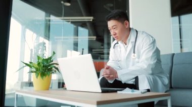 Asyalı doktor hastaya internet üzerinden bilgisayar ve webcam kullanarak görüntülü görüşme öneriyor. Uzaktan bir doktorla görüşeceğim. Adam iş arkadaşlarıyla konuşuyor. Teletıp, tele-sağlık. Modern cerrahi ofisi