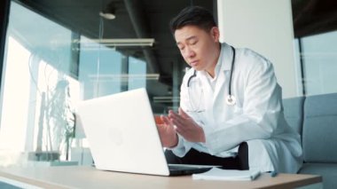 Asyalı doktor hastaya internet üzerinden bilgisayar ve webcam kullanarak görüntülü görüşme öneriyor. Uzaktan bir doktorla görüşeceğim. Adam iş arkadaşlarıyla konuşuyor. Teletıp, tele-sağlık. Modern cerrahi ofisi