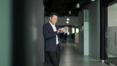 Ciddi Asyalı erkek işçi modern ofiste tablet bilgisayarla çalışmaya odaklanmış. İşadamı profesyonel girişimci CEO finans müdürü Smartphone online yatırım borsasını kullanıyor