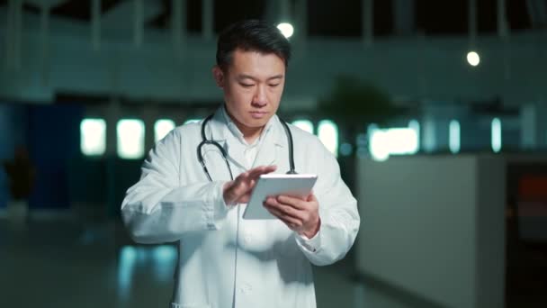 Asian Doctor Uses Tablet Computer While Standing Modern Hospital Clinic — 图库视频影像