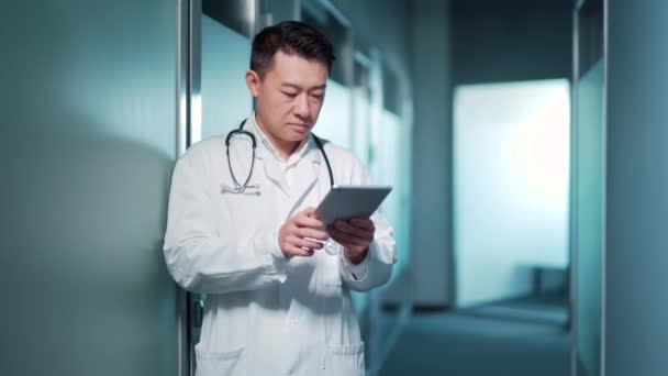 Asian Doctor Uses Tablet Computer While Standing Modern Hospital Clinic — 图库视频影像