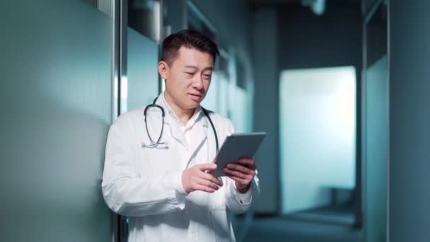 亚洲男医生建议病人远程使用数码平板电脑 在一家现代化的医院诊所里 通过视频通话进行在线交流 男医生处方治疗 远程医疗 — 图库视频影像