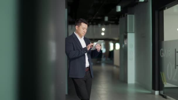 严肃的亚裔男性员工专注于现代办公室的平板电脑工作 使用Smartphone在线投资股票的商人 专业企业家和财务经理经纪人 — 图库视频影像