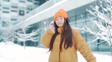 Genç, güzel bir Asyalı kadın kulaklıklardan müzik dinliyor. Kışın karlı bir günde yürüyor. İnternette bir uygulama kullanıyor. 