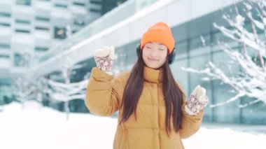 Genç, güzel bir Asyalı kadın kulaklıklardan müzik dinliyor. Kışın karlı bir günde yürüyor. İnternette bir uygulama kullanıyor. 