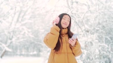 Neşeli, komik Asyalı ergen kız öğrenci karlı bir kış gününde parkta müzik dinleyerek yürüyor. Cep telefonu olan genç bir kadın soğuk havada dans etmekten hoşlanır. Dışarıda.