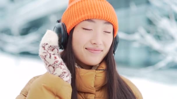아름다운 아시아 여성은 눈내리는 헤드폰을 음악을 온라인 사용하며 날씨가 소녀가 — 비디오