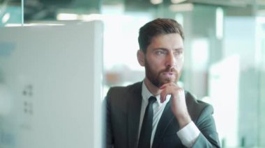 Modern bir ofis masasında bilgisayar üzerinde çalışan düşünceli bir erkek işadamı portresi. Takım elbiseli, dalgın, düşünceli bir iş adamı. Bir sorunu çözmek için ilham almayı düşünüyorum. Açılış