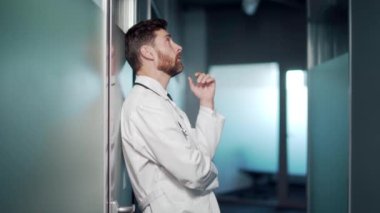 Stresli bir doktorun portresi hastane koridorunda duruyor. Klinikte düşünceli, düşünceli bir doktor. Salgın sırasında steteskopla önlük giyen erkek hasta bakıcısı stresi.